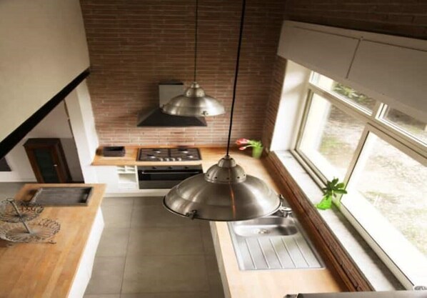 A modern kitchen with a brick backsplash, stainless steel appliances, and a pendant light.