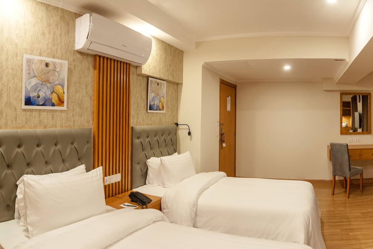 Habitación de hotel con dos camas, un escritorio, una silla, un televisor y un reloj en la pared.