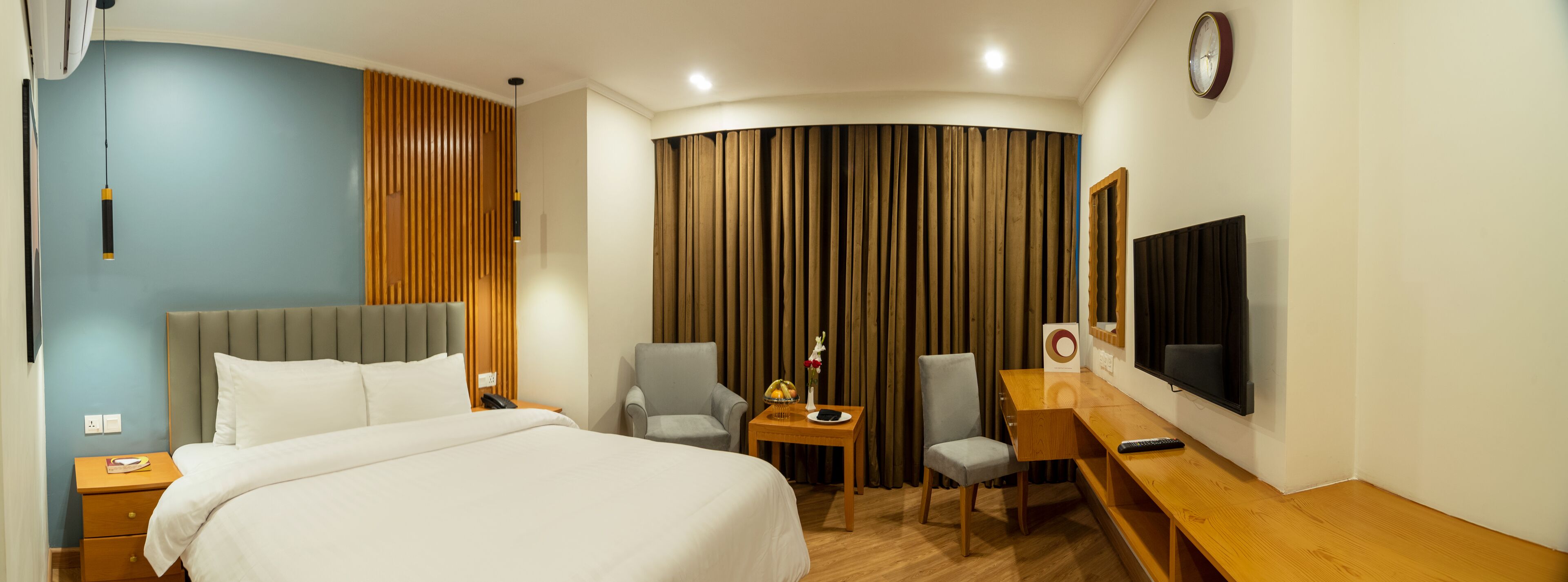 A hotel room with a bed, two chairs, a desk, a TV, and a curtain.