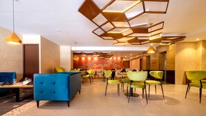 En rymlig entréhall med moderna möbler, inklusive en blå soffa och gröna stolar, samt en takdesign med geometriska mönster.