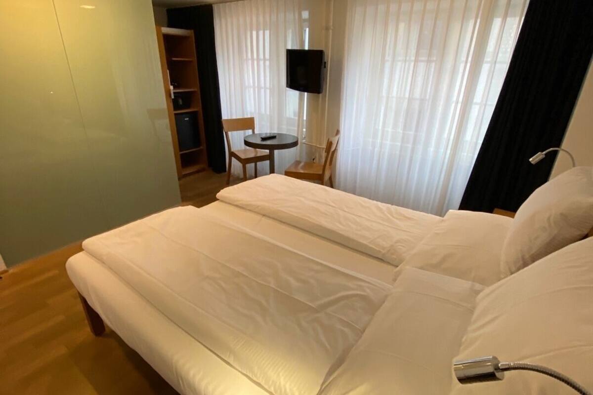 A hotel room with a large bed, a TV mounted on the wall, and a small table with chairs.