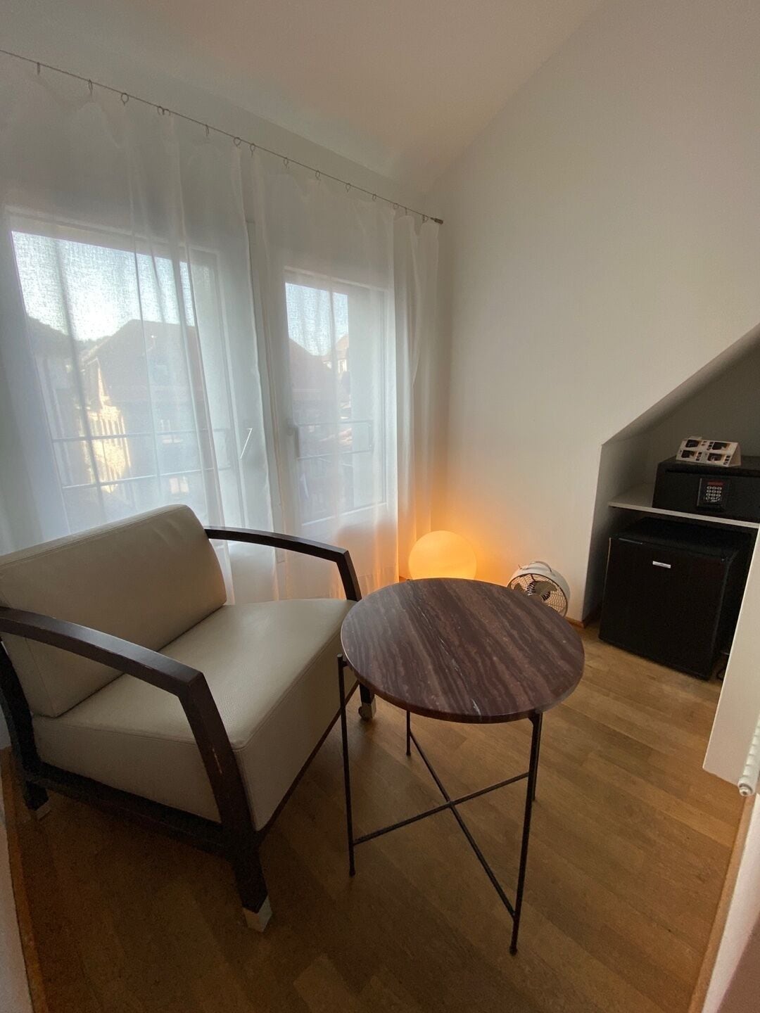 Una habitación pequeña y acogedora con un sofá, una mesa redonda, una lámpara y un armario pequeño.
