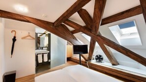 Un dormitorio con techo inclinado, vigas de madera, una cama, un televisor y una ventana.