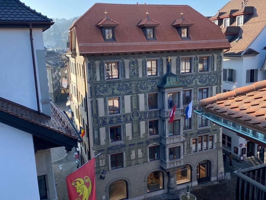 Un edificio histórico con fachadas ornamentadas y numerosas ventanas, situado en una zona urbana densamente construida.