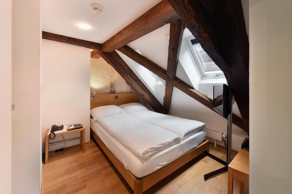 Un dormitorio con cama de madera, una mesita de noche con lámpara y un tragaluz.