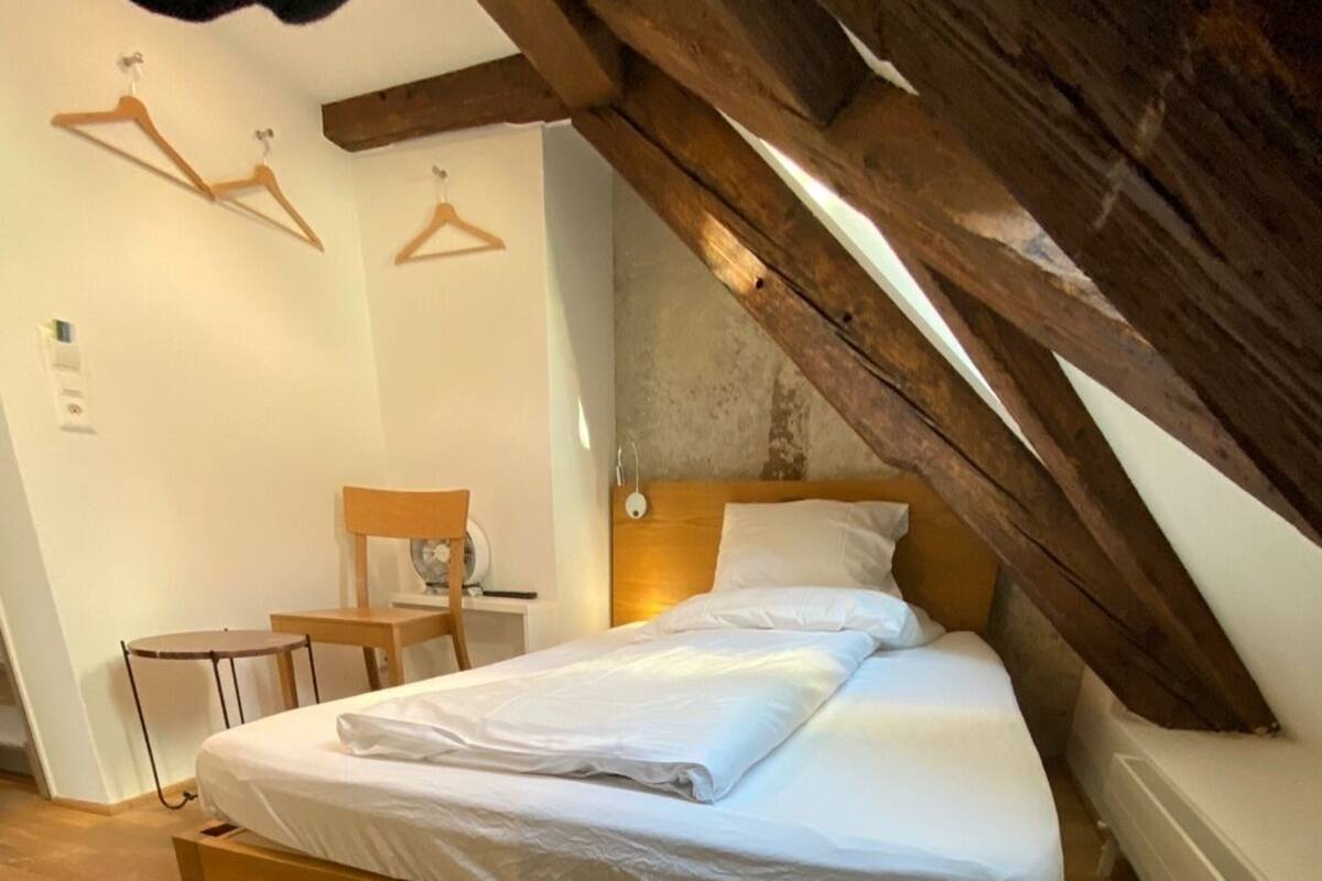 A bedroom with a wooden bed, a wooden chair, a small table, and a wall-mounted heater.
