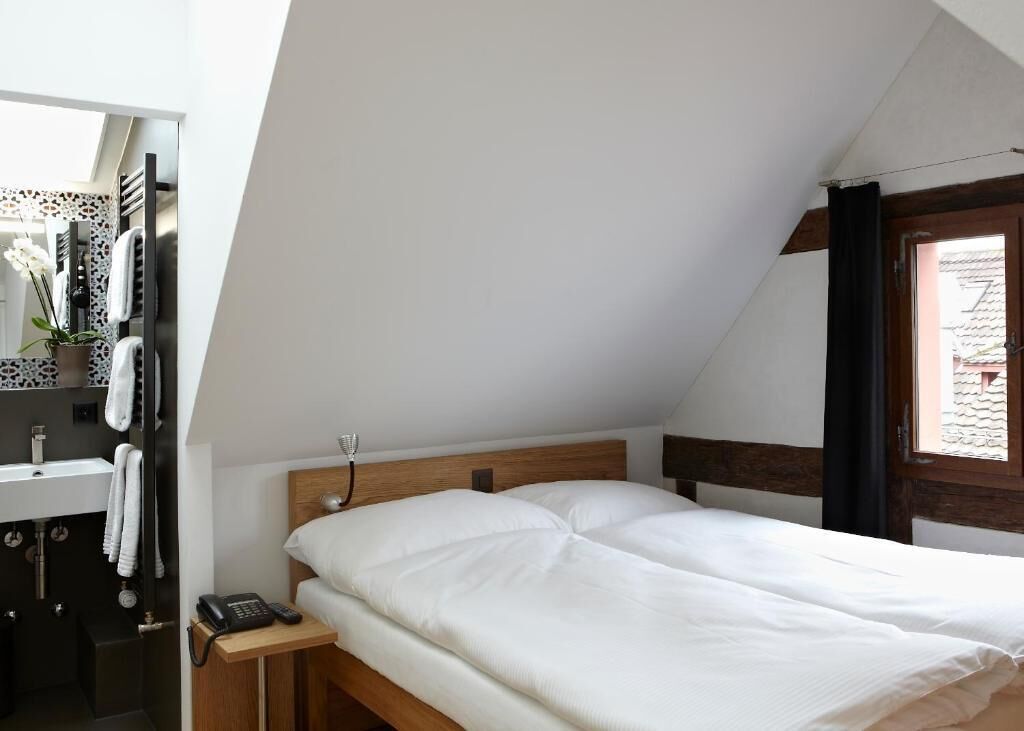 Ein Schlafzimmer mit einem hölzernen Kopfende, einem Nachttisch mit Telefon und einem fenster mit Vorhängen.