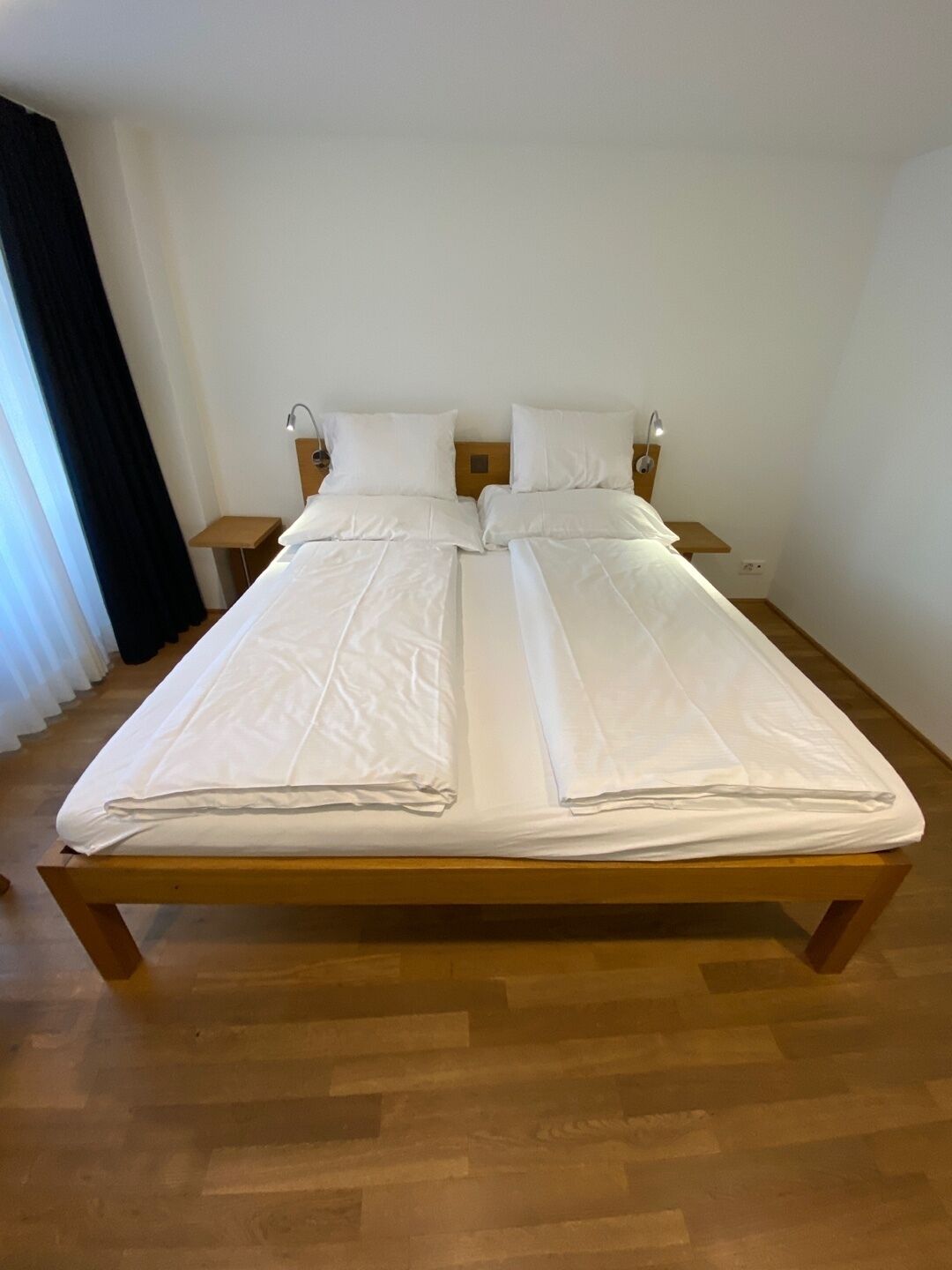 A double bed with white linens, two bedside tables with lamps, and a wooden floor.