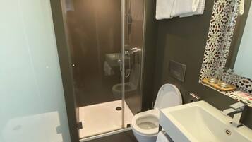 Un baño moderno con ducha envuelta en vidrio, inodoro blanco y tocador con lavamanos.