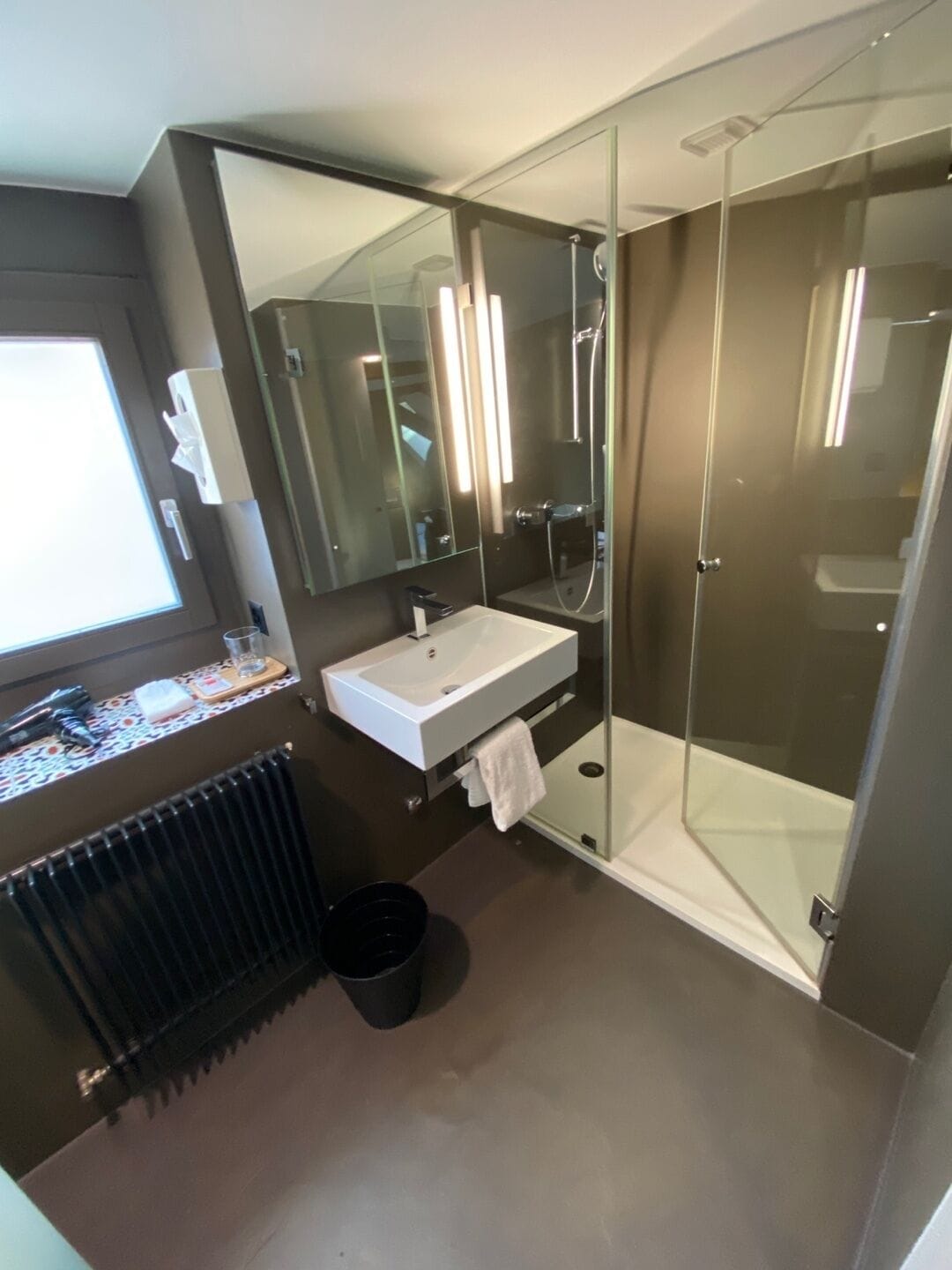 Ein modernes Badezimmer mit einer Duschkabine aus Glas, einem weißen Waschbecken und einem großen Spiegel.