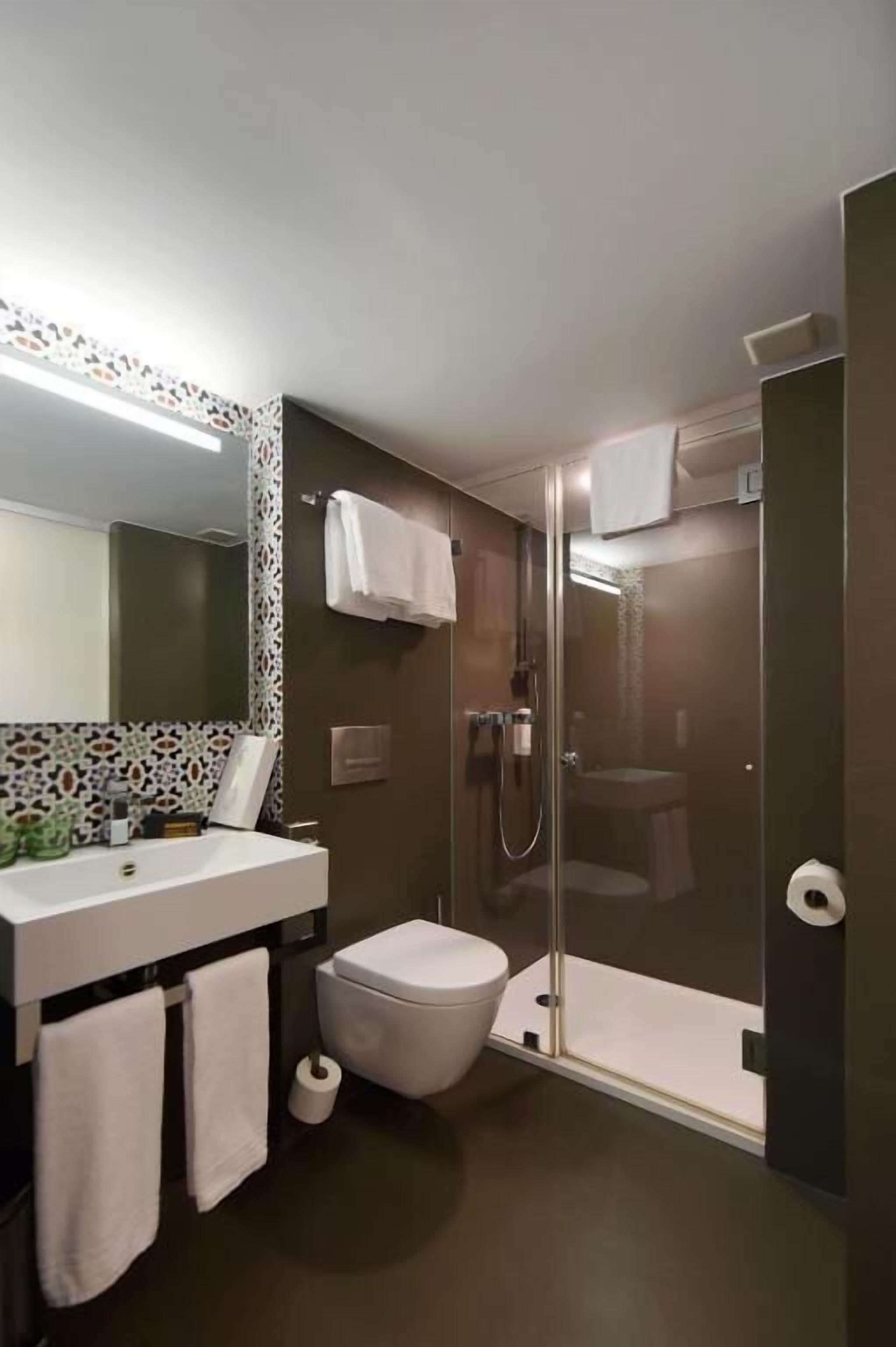 Un baño moderno con ducha envuelta en vidrio, inodoro blanco y tocador con espejo y toallero.