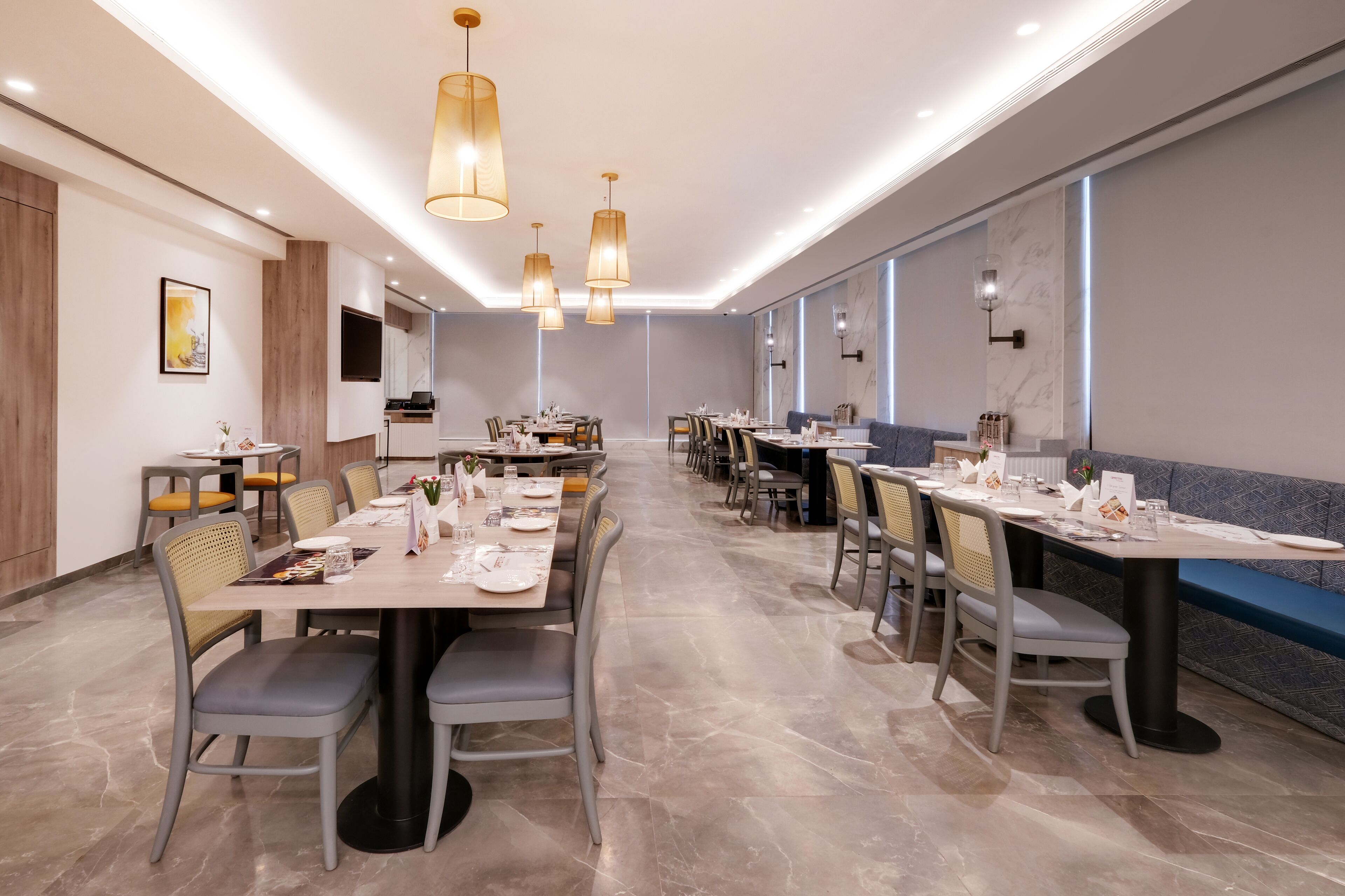 A modern dining area with multiple tables and chairs, recessed ceiling lighting, and a large window providing natural light.