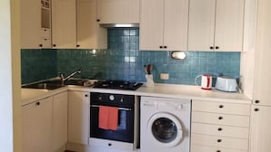 A compact kitchen with white cabinets, a blue tiled backsplash, a built-in oven, a washing machine, and a coffee maker. - The villett 🏡 in the countryside a stone's throw from the sea (Pescia Romana)