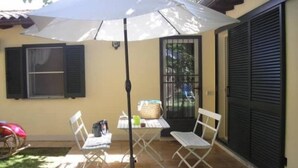 An outdoor patio with a table and two chairs, a white umbrella, and a red scooter. - The villett 🏡 in the countryside a stone's throw from the sea (Pescia Romana)