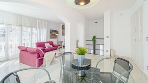 Una sala de estar moderna con una mesa de comedor de vidrio, un sofá rosa y un ventanal grande.