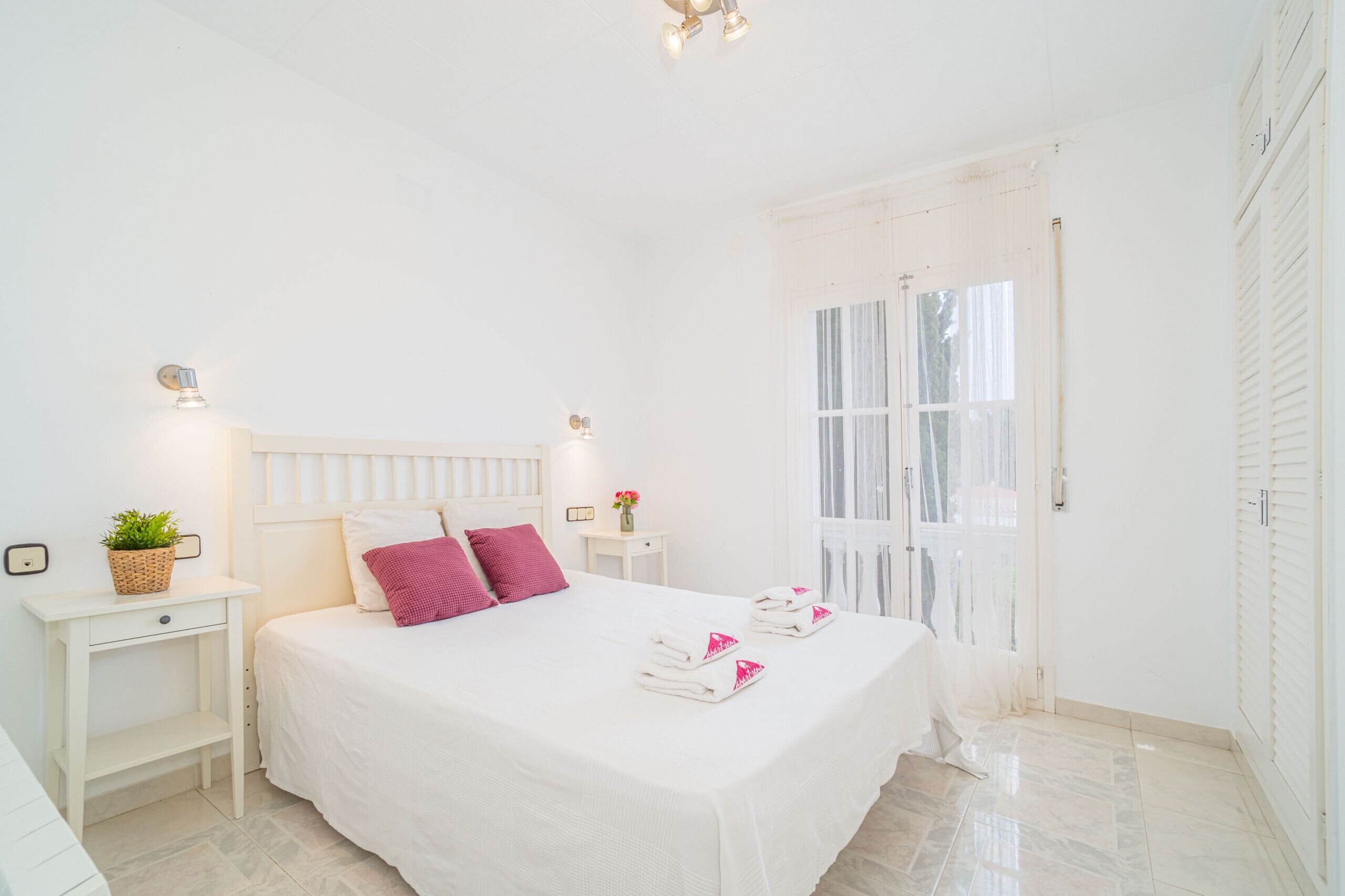 A white bedroom with a bed, bedside tables, a window, and a door.