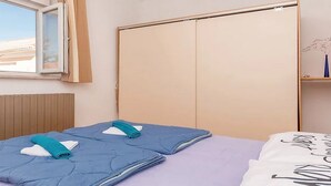 A bedroom with a bed, a window with curtains, a wardrobe, and a shelf with a vase. - Apartment Marjan (Posedarje)