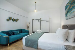 Un dormitorio moderno con un sofá azul aguamarina, una cama con ropa blanca y una lámpara colgante, además de un adorno en la pared.