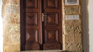 Eine hölzerne Doppeltür unter einem steinernen Rundbogen, ein Schild mit 'Rodos Property' und der Aufschrift 'Luxury Suites' sowie eine kleine Plakette mit vier Symbolen.