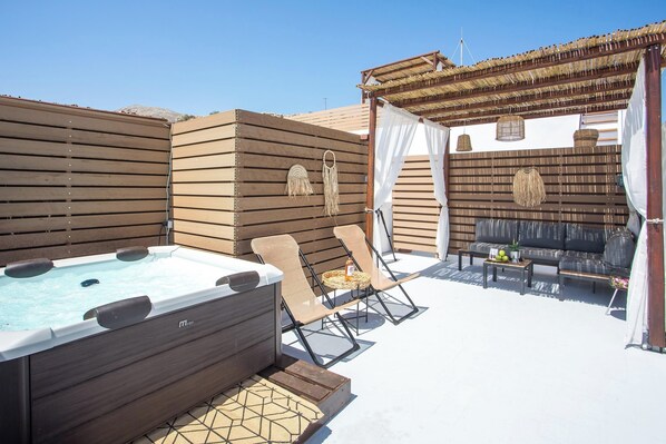 Terraza en la azotea con un jacuzzi, sillas de descanso y un área de estar con cojines y una mesa.
