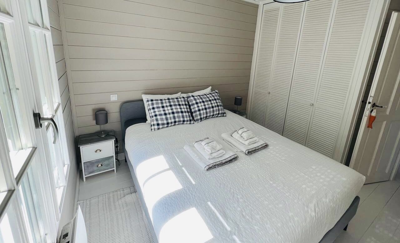 Una cama bien hecha con edredón blanco y dos almohadas, una mesita de noche con lámpara y un armario con puertas correderas.