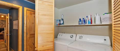 Un área de lavandería con una puerta de madera, una lavadora y estantes con productos de limpieza.