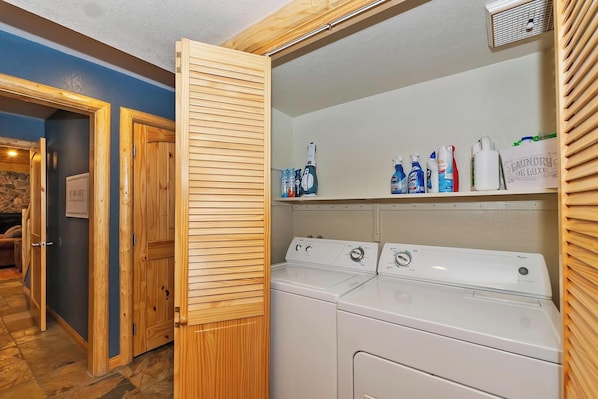Un espace buanderie avec une porte en bois, un lave-linge et des étagères remplies de produits de nettoyage.