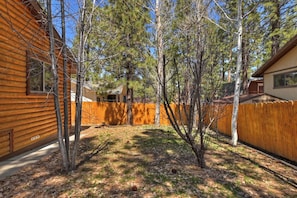 Une cabane en bois avec un jardin clôturé, entourée d’arbres.
