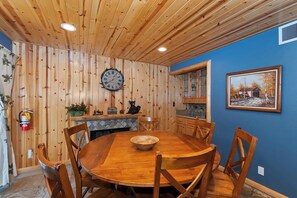A wooden dining room with a round table and chairs, a clock on the wall, a fire extinguisher, and a painting on the wall. - Situated in the Heart of Big Bear! Fully Fenced Yard! Pool Table! EV Charger! (Big Bear Lake)