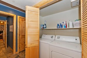 Une buanderie équipée d’un lave-linge et d’un sèche-linge, de placards en bois et d’une étagère contenant des produits de nettoyage.
