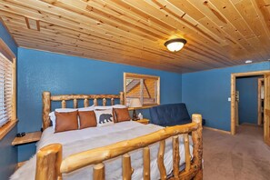 Een kamer met een houten bed, nachtkastje, lamp en raam met jaloezieën.