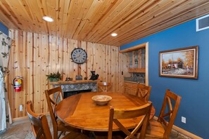 A wooden-paneled room with a round wooden table and chairs, a clock on the wall, and a framed picture. - Situated in the Heart of Big Bear! Fully Fenced Yard! Pool Table! EV Charger! (Big Bear Lake)