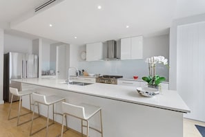 A modern kitchen with a central island, bar stools, stainless steel appliances, and a potted orchid.