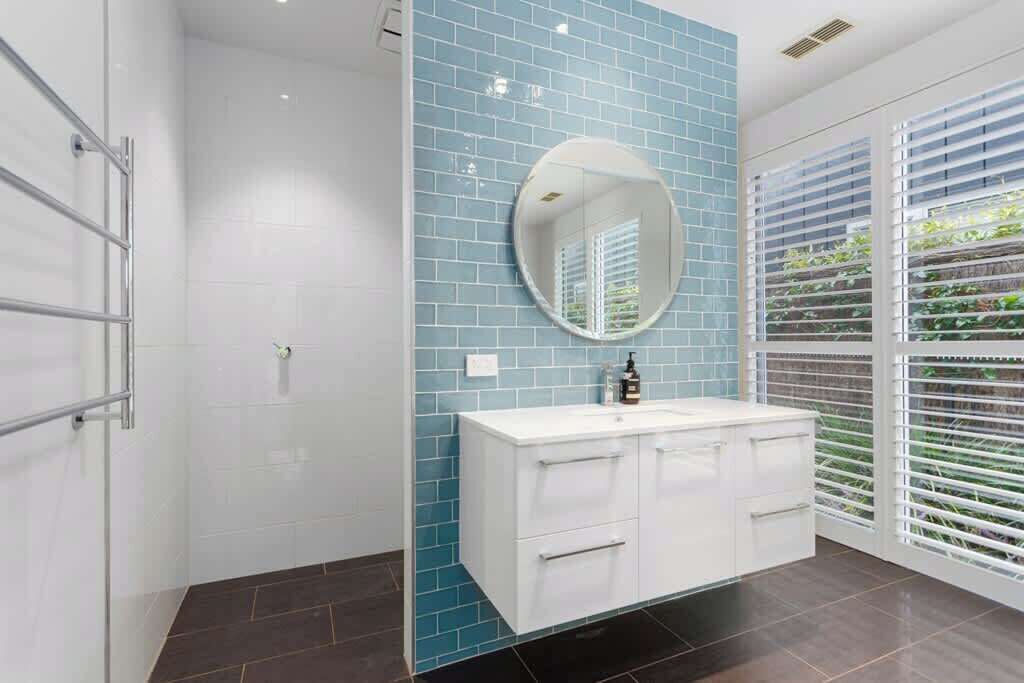 Un baño con un tocador blanco, un espejo redondo y una pared con azulejos azules.