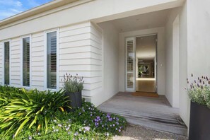 A modern house with a wooden deck, a covered entryway, and a garden with various plants and flowers.