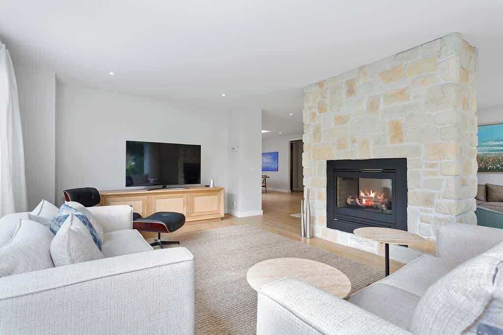 A modern living room with a stone fireplace, a flat-screen TV, and a sofa.