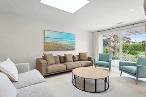 A modern living room with a sofa, armchairs, a coffee table, and a large window with a view of greenery.