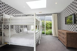 A bunk bed room with a large window, a TV, and a wooden dresser. - Banksia House (Blairgowrie)