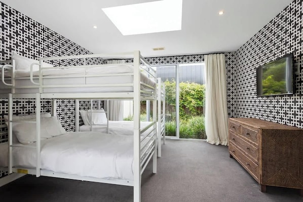 A bunk bed room with a large window, a TV, and a wooden dresser. - Banksia House (Blairgowrie)