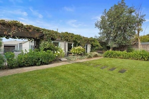 A well-maintained backyard with a lawn, a pergola covered in greenery, and a large tree. - Banksia House (Blairgowrie)