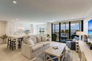 Enjoy a comfortable stay in this apartment with a spacious living area, dining table, and kitchen with white cabinetry, plus a large balcony with sea views.