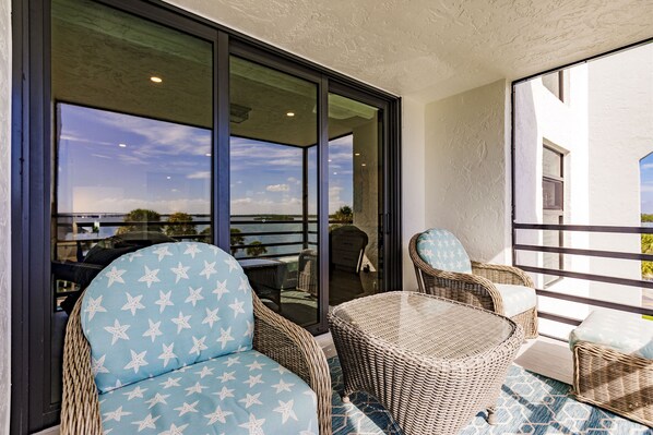 Relax on the balcony with a view of the surrounding landscape, featuring a wicker chair and table.