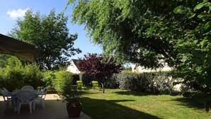 Eine Terrasse mit Tisch und Stühlen, umgeben von Grünpflanzen und einem Baum.