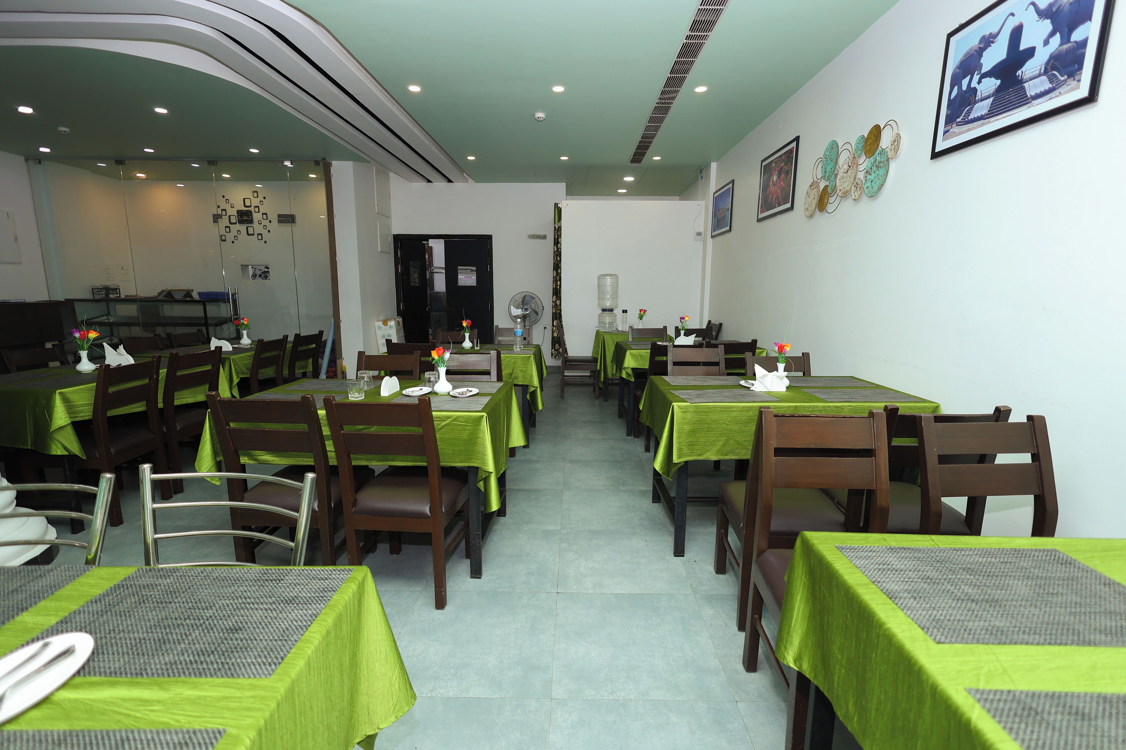 Un restaurant dont les tables sont recouvertes de nappes vertes, avec des chaises en bois et un sol carrelé.