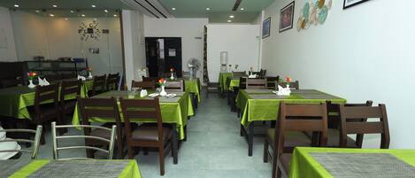 Un restaurant dont les tables sont recouvertes de nappes vertes, avec des chaises en bois et un sol carrelé.