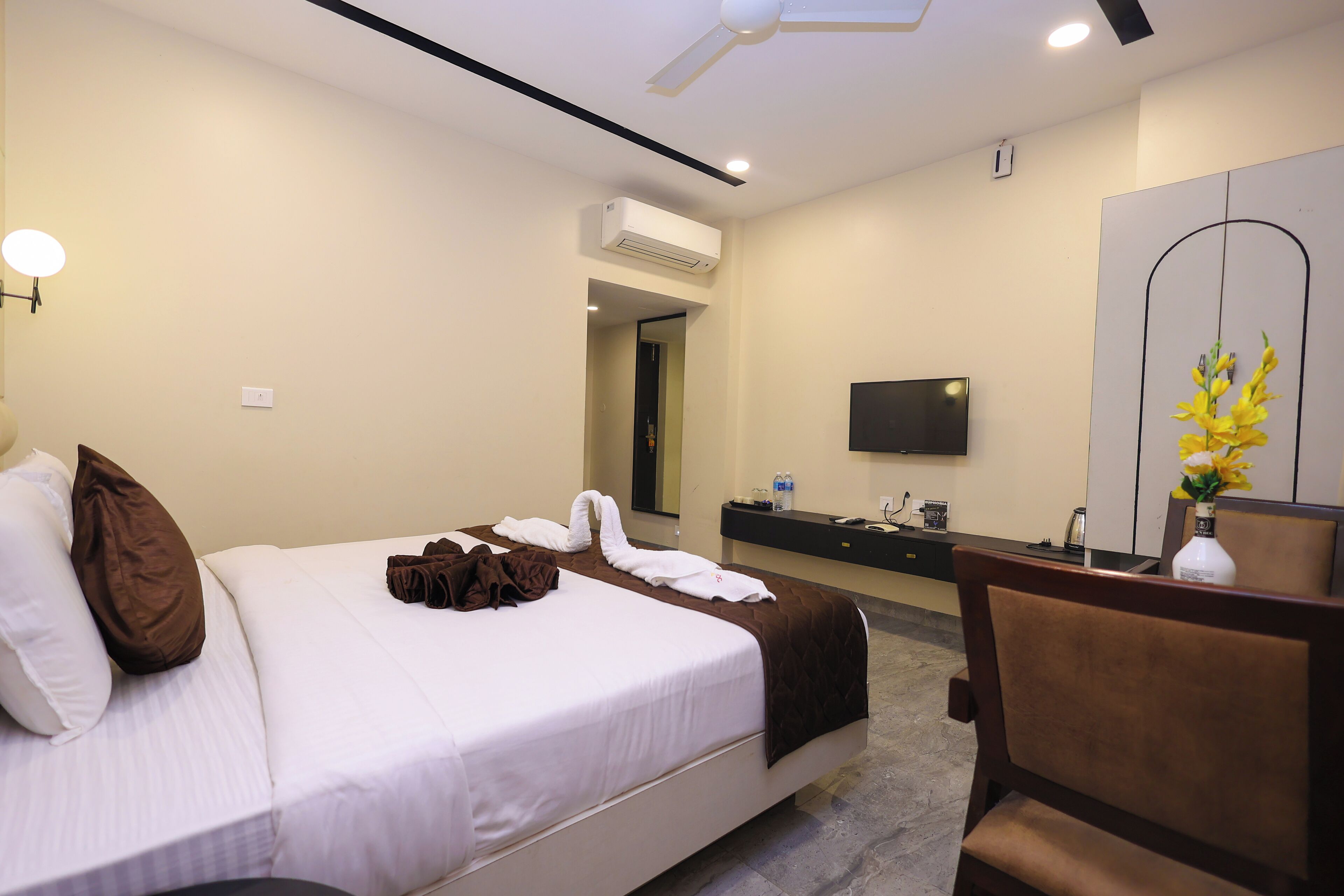 Una habitación de hotel con cama, escritorio, silla, televisor y espejo.