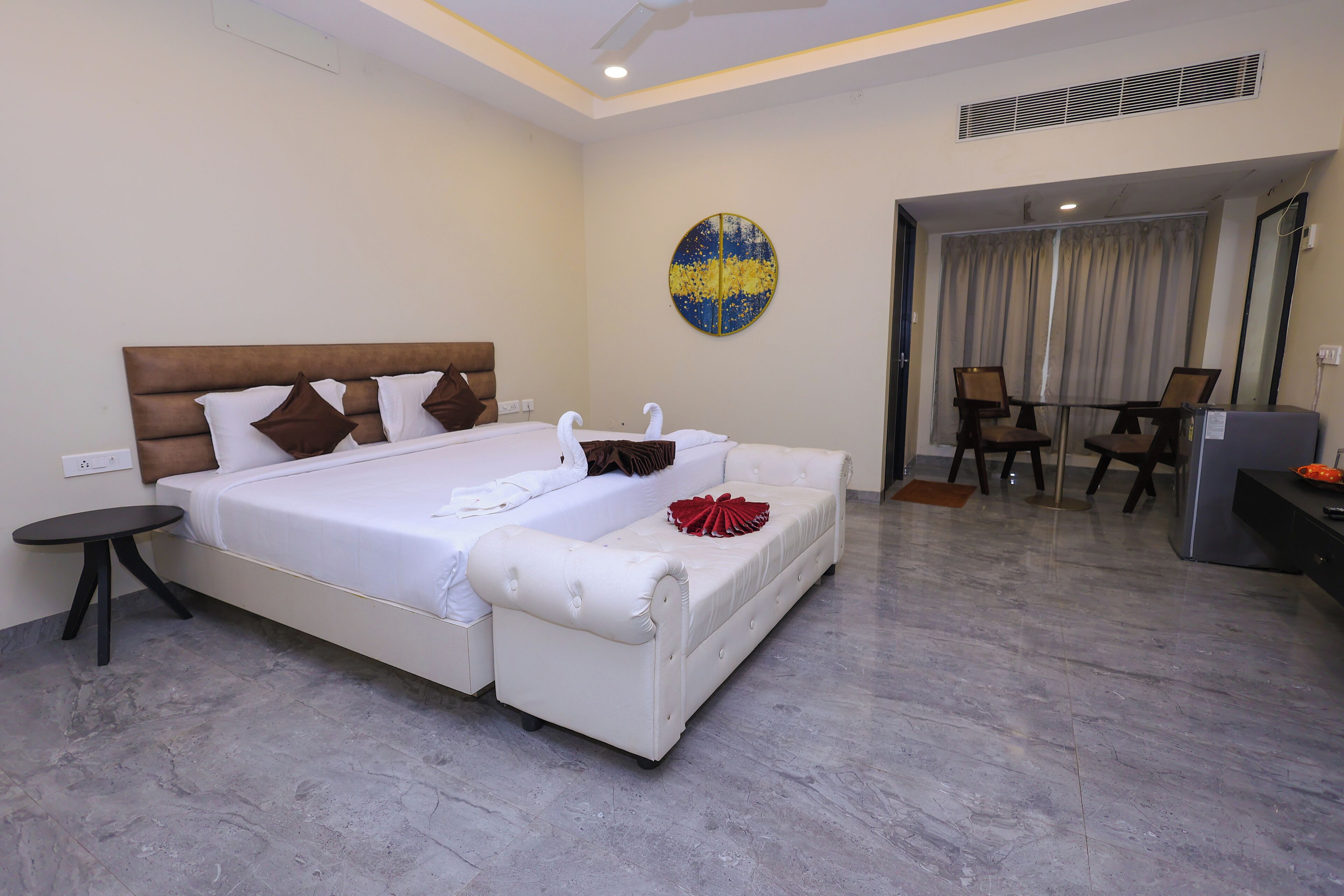 Quarto de hotel com uma cama grande, uma pequena mesa redonda, um sofá e uma área de refeições com cadeiras.