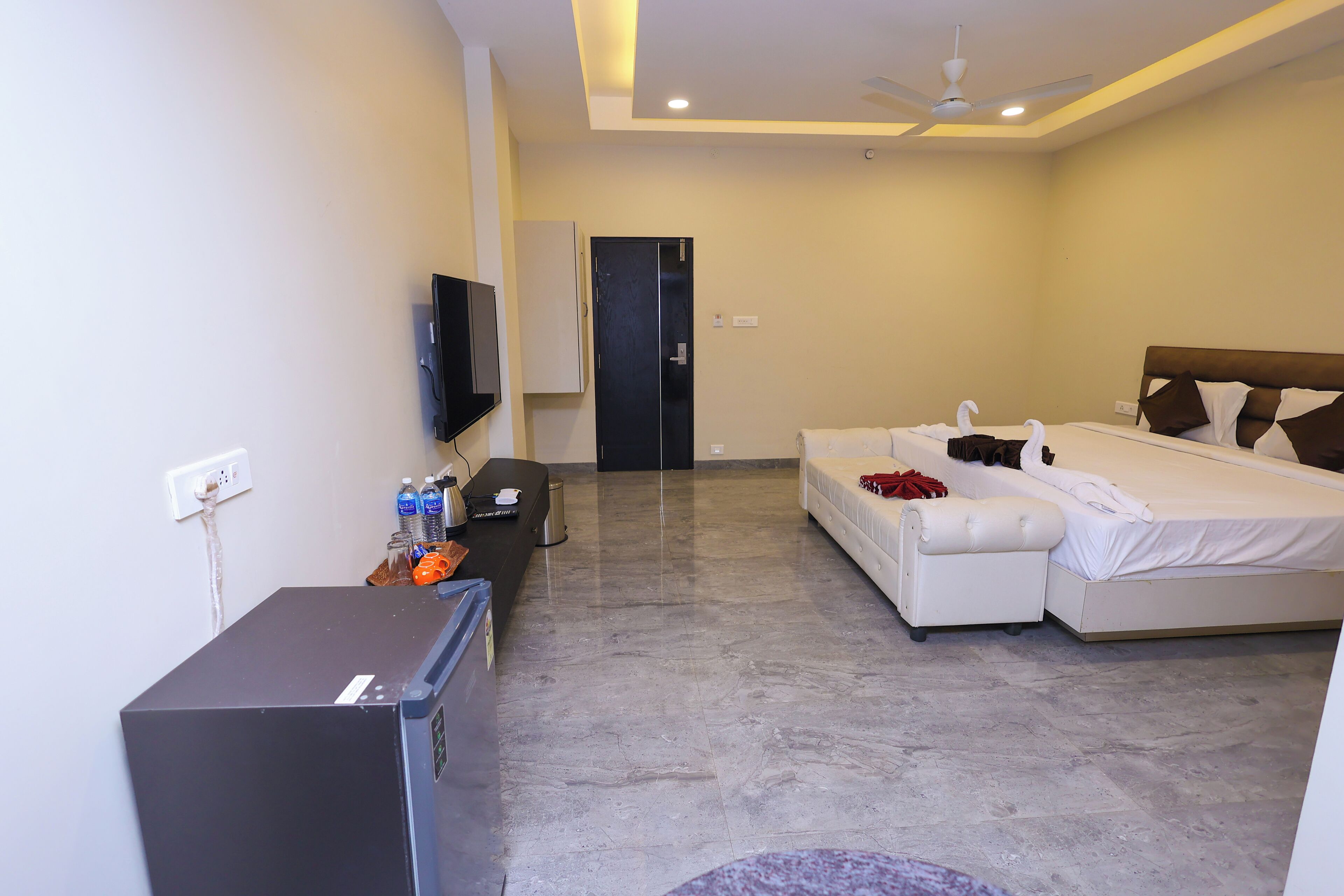 Habitación de hotel con cama, sofá, televisor, escritorio con computadora y ventilador de techo.