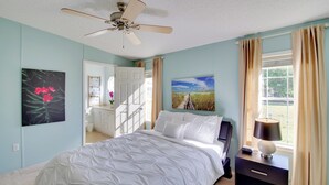 Een slaapkamer met een bed, een nachtkastje met een lamp, een plafondventilator en twee schilderijen aan de wanden.