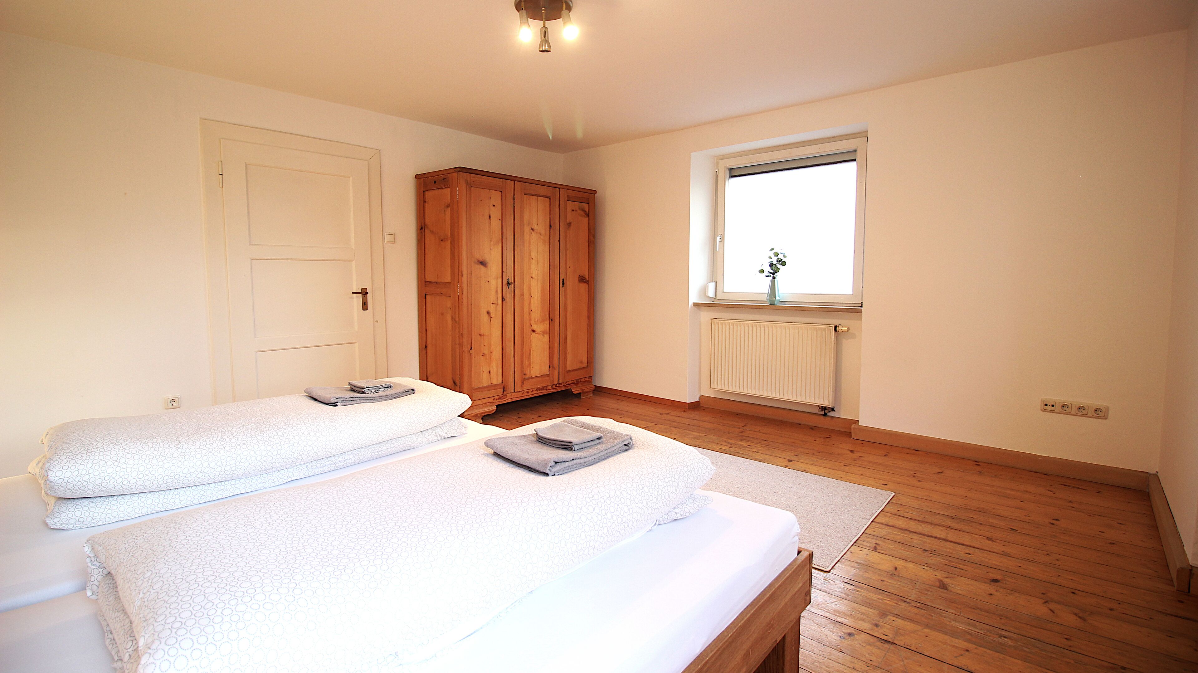Une chambre avec deux lits, une armoire en bois, une fenêtre avec vue et un radiateur.